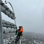 Rope access electrician replacing floodlight lamps high on a stadium pylon