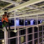Rope access technician suspended under the steel atrium roof at Leonardo Royal Hotel St Paul's at night