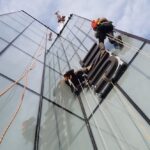 Sign installation by rope access: fitting Unite Students letters on a glass facade alongside a crane
