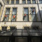 Rope access building maintenance team of four technicians abseiling a brick building facade